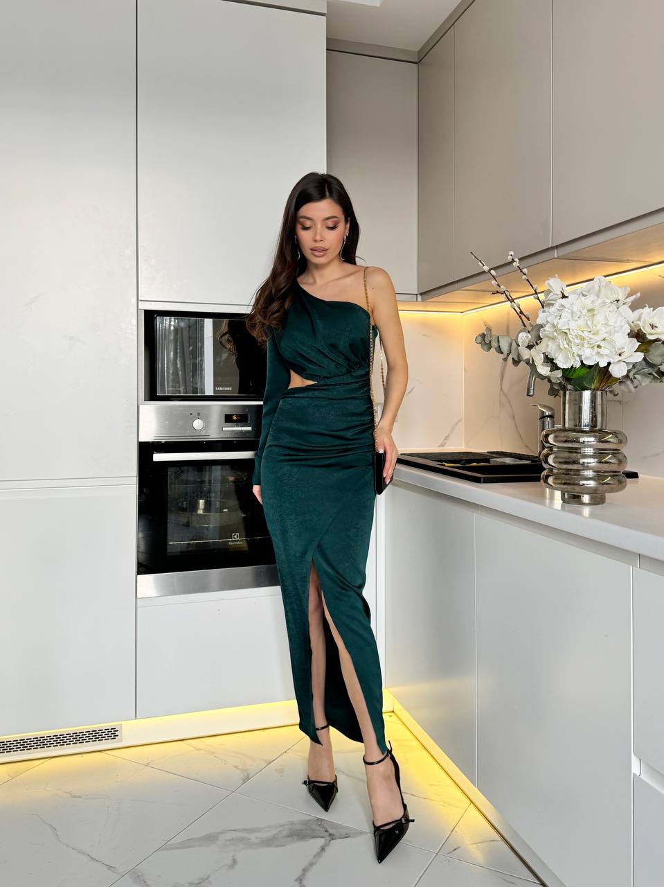 Woman in a green dress standing in a modern kitchen.