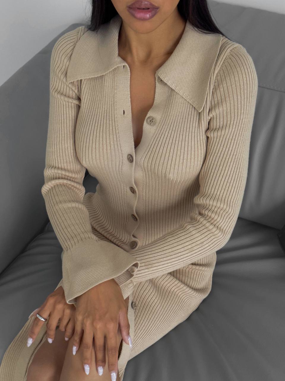 Woman wearing a beige ribbed sweater dress sitting on a gray couch.