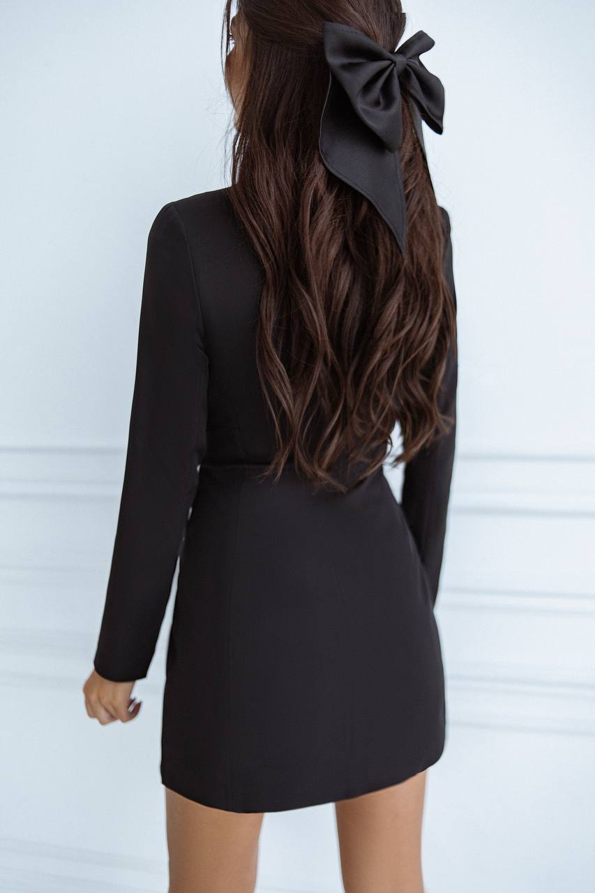 Person wearing a black dress with long sleeves and a large black bow in their hair against a white background