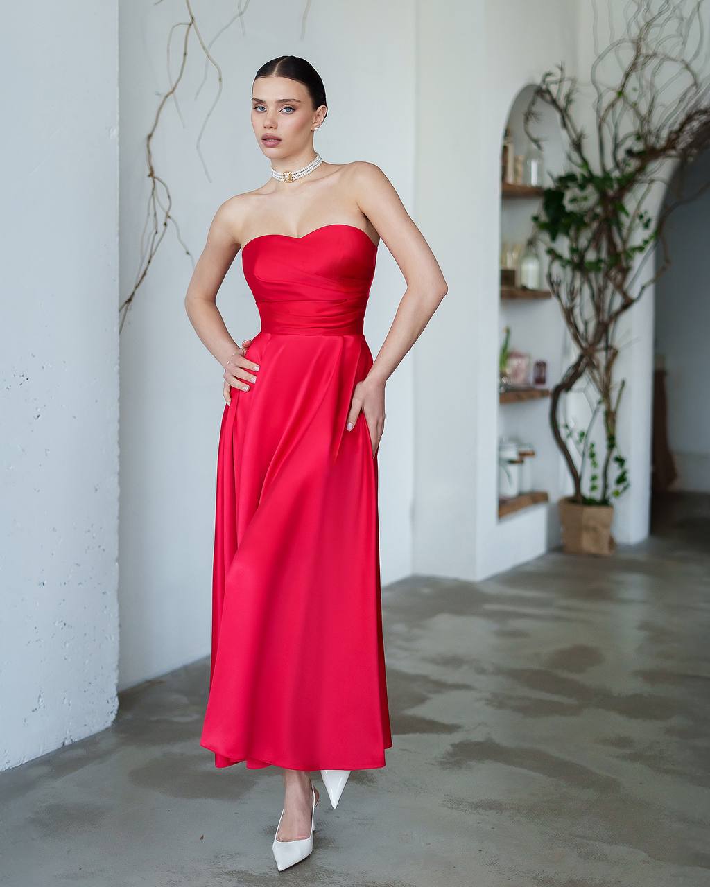 Woman wearing a red strapless dress in an indoor setting with white walls and minimal decor.