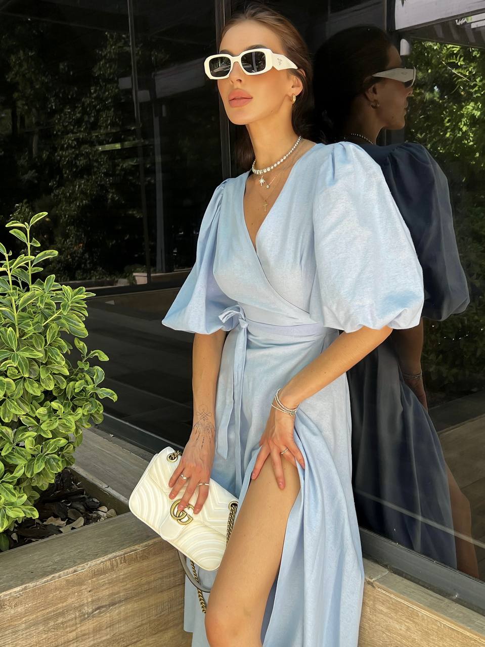 Woman in a light blue dress with puffed sleeves standing outdoors.