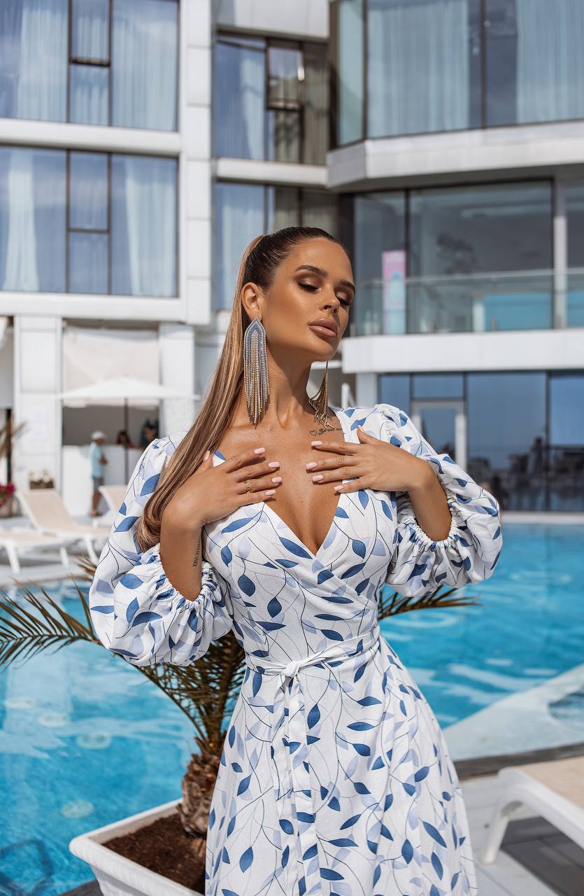 Woman in a blue and white patterned dress standing by a pool with a modern building in the background