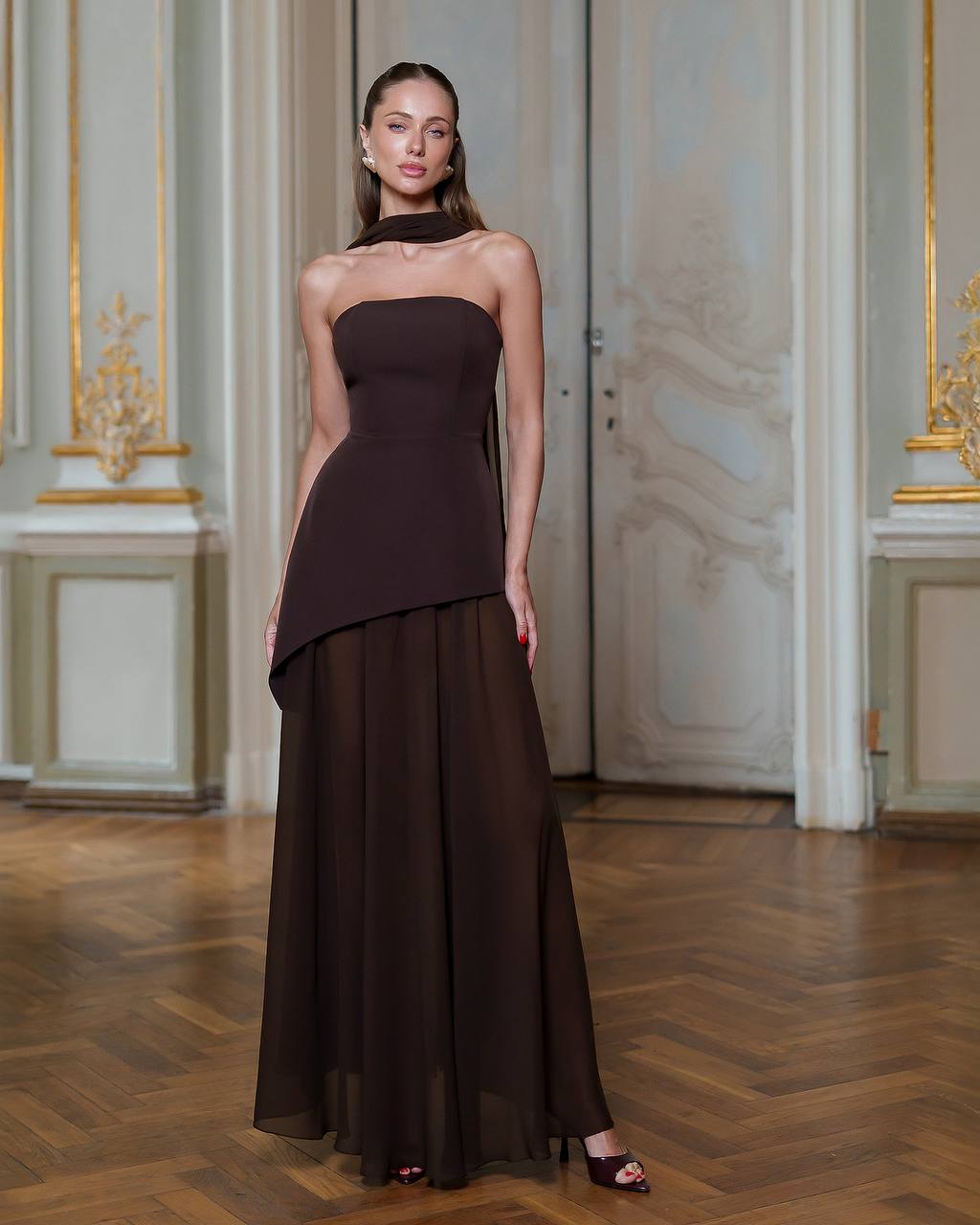Woman wearing a dark brown strapless gown in an elegant interior setting.