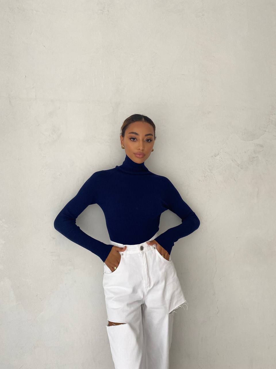 Person wearing a navy turtleneck and white pants against a plain background