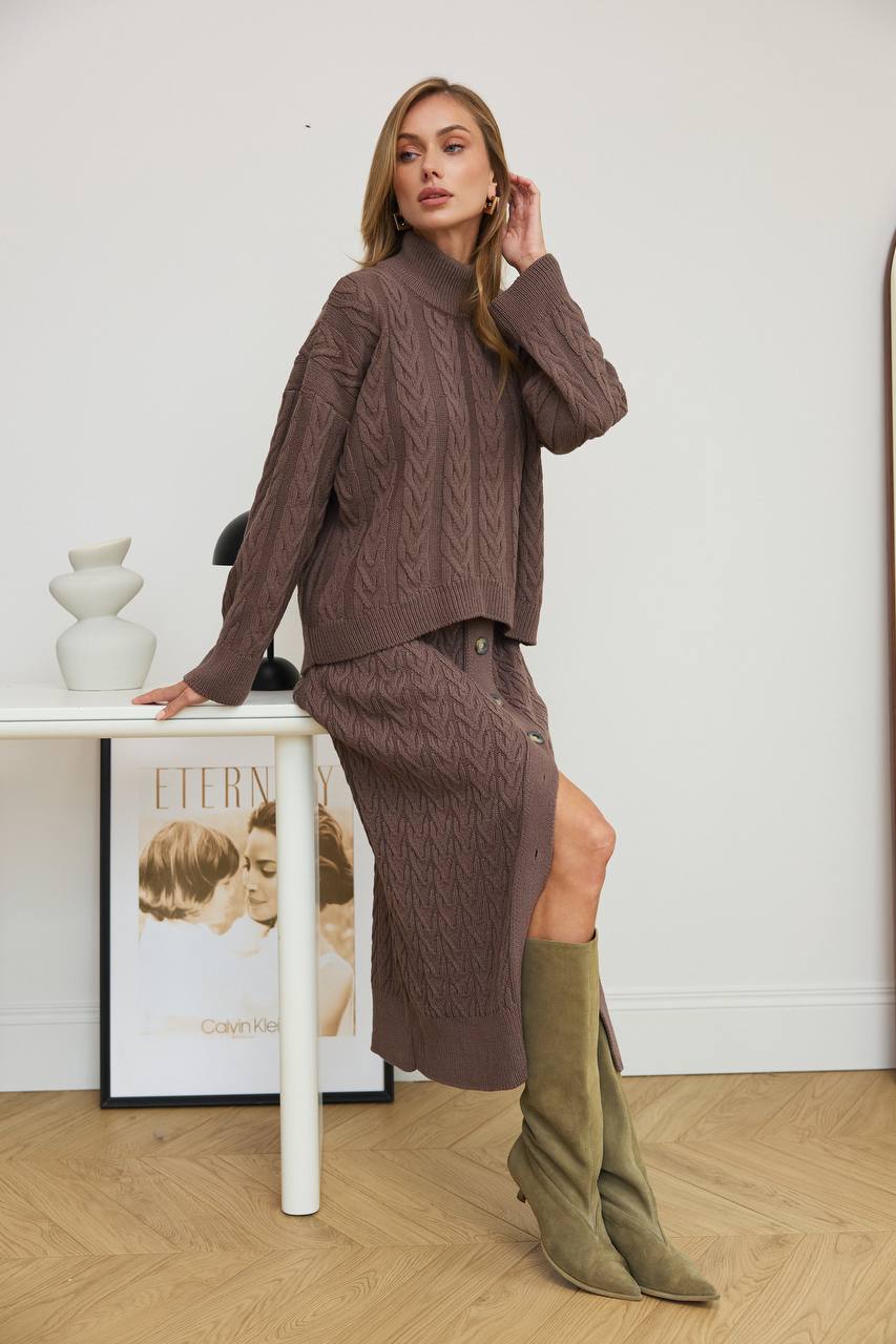 Woman in a brown outfit with green boots standing by a white table.