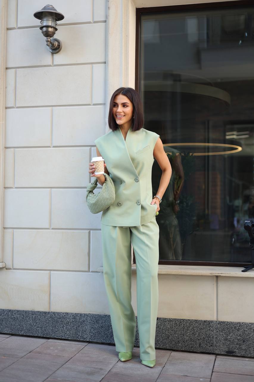 Woman in a light green suit standing outside a building holding a coffee cup.