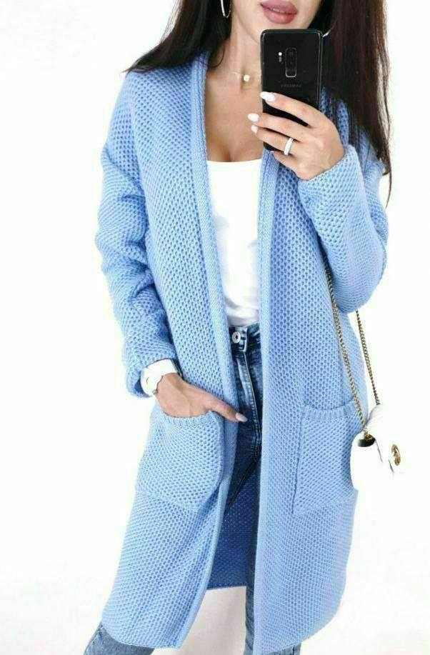 Person wearing a light blue cardigan with a white top and jeans, holding a phone.