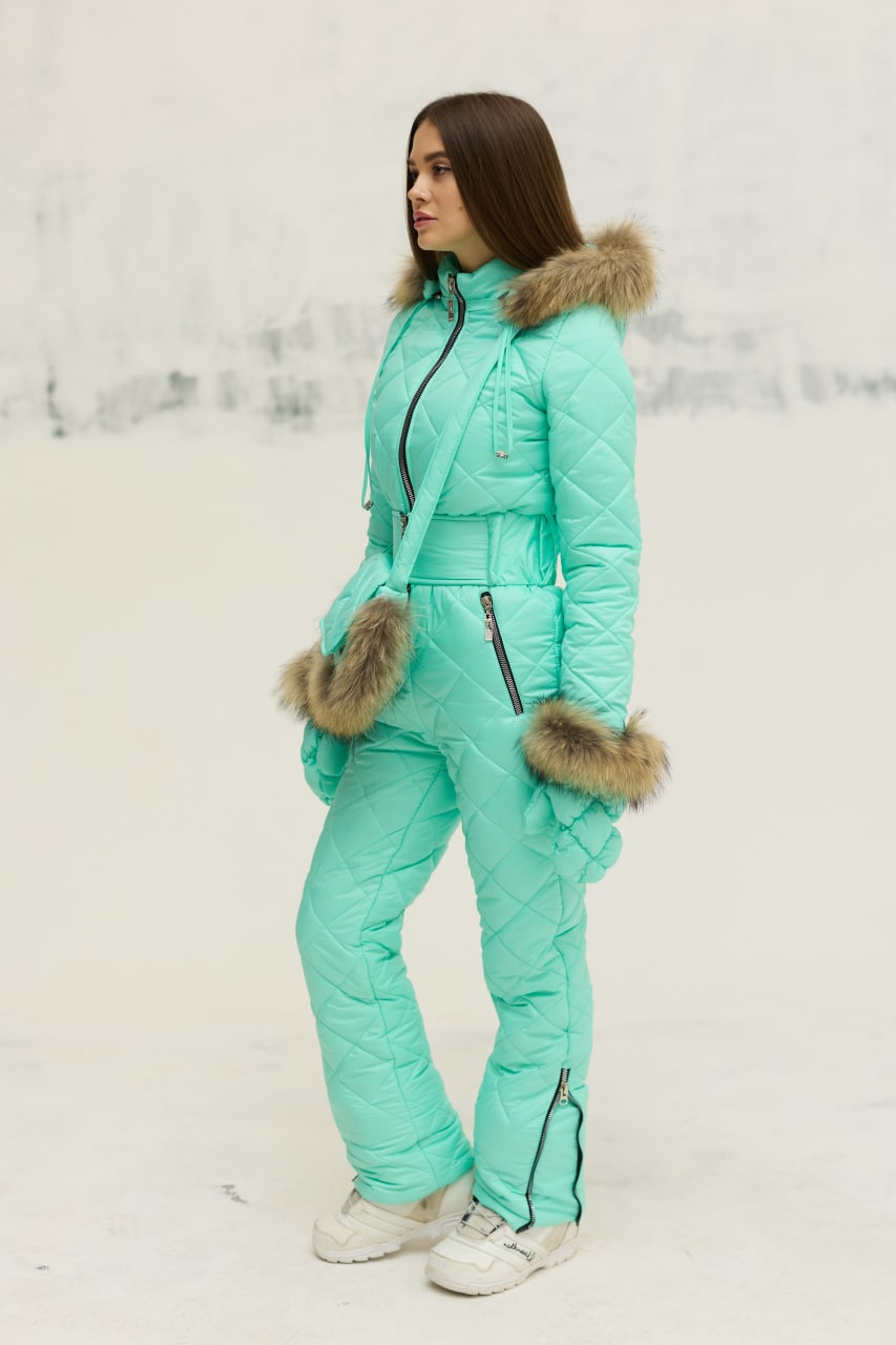 Person wearing a turquoise winter outfit with fur trim on a light background