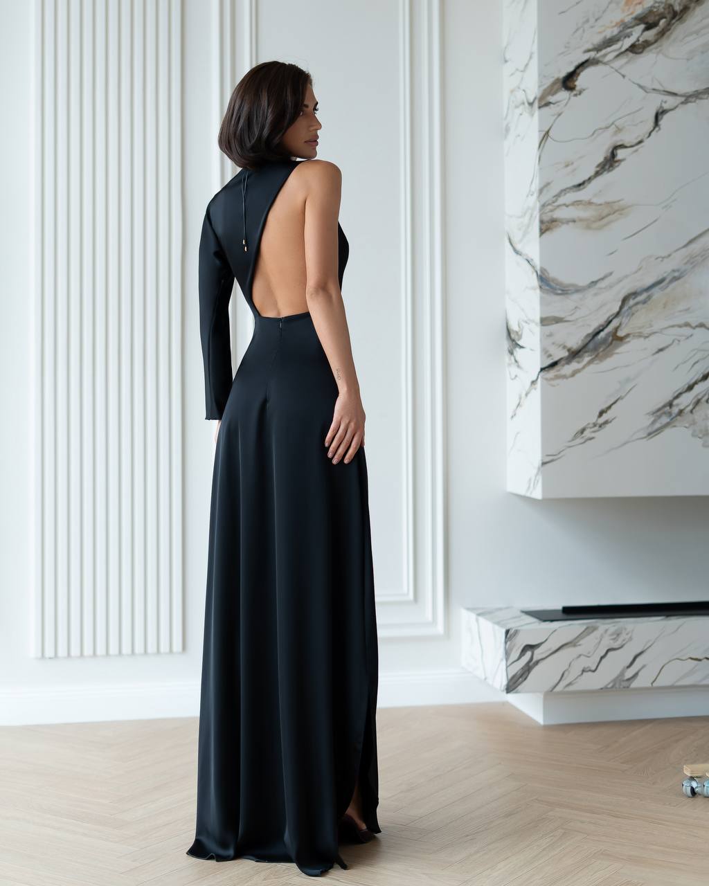 Woman in a black evening gown with an open back in a stylish interior setting.