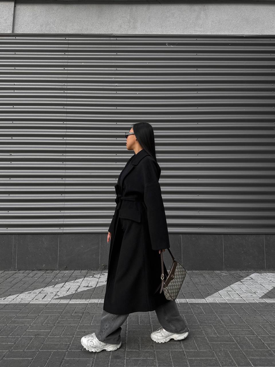 Person wearing a black coat and gray pants walking past a closed shutter.