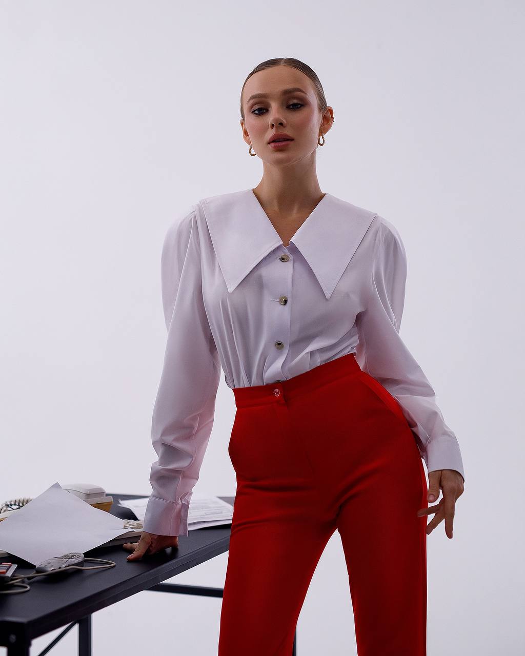 Woman wearing a white blouse and red pants against a white background