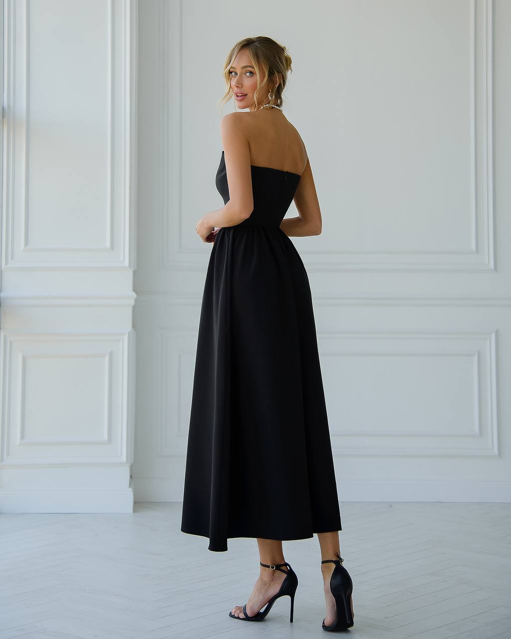 Woman wearing a black strapless dress in a minimalistic room.