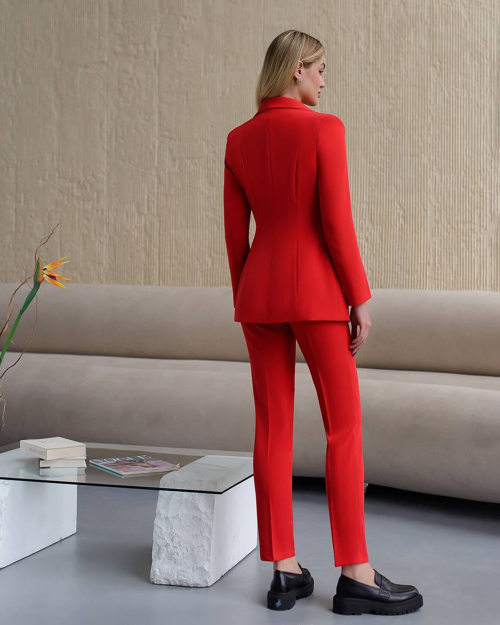Woman in a red suit standing in a modern living room.