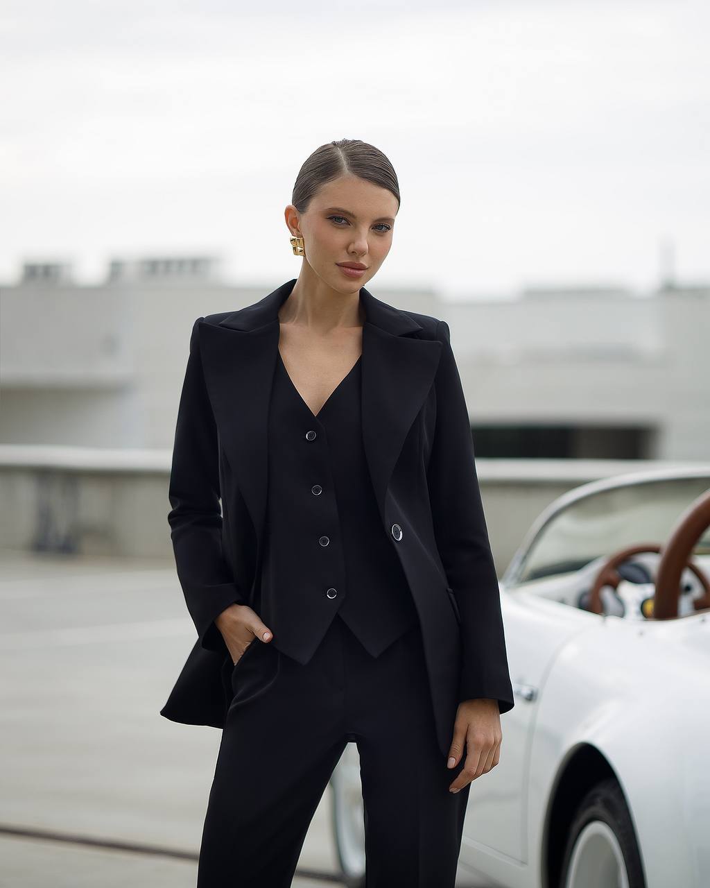 Woman in a black suit standing in front of a vintage car
