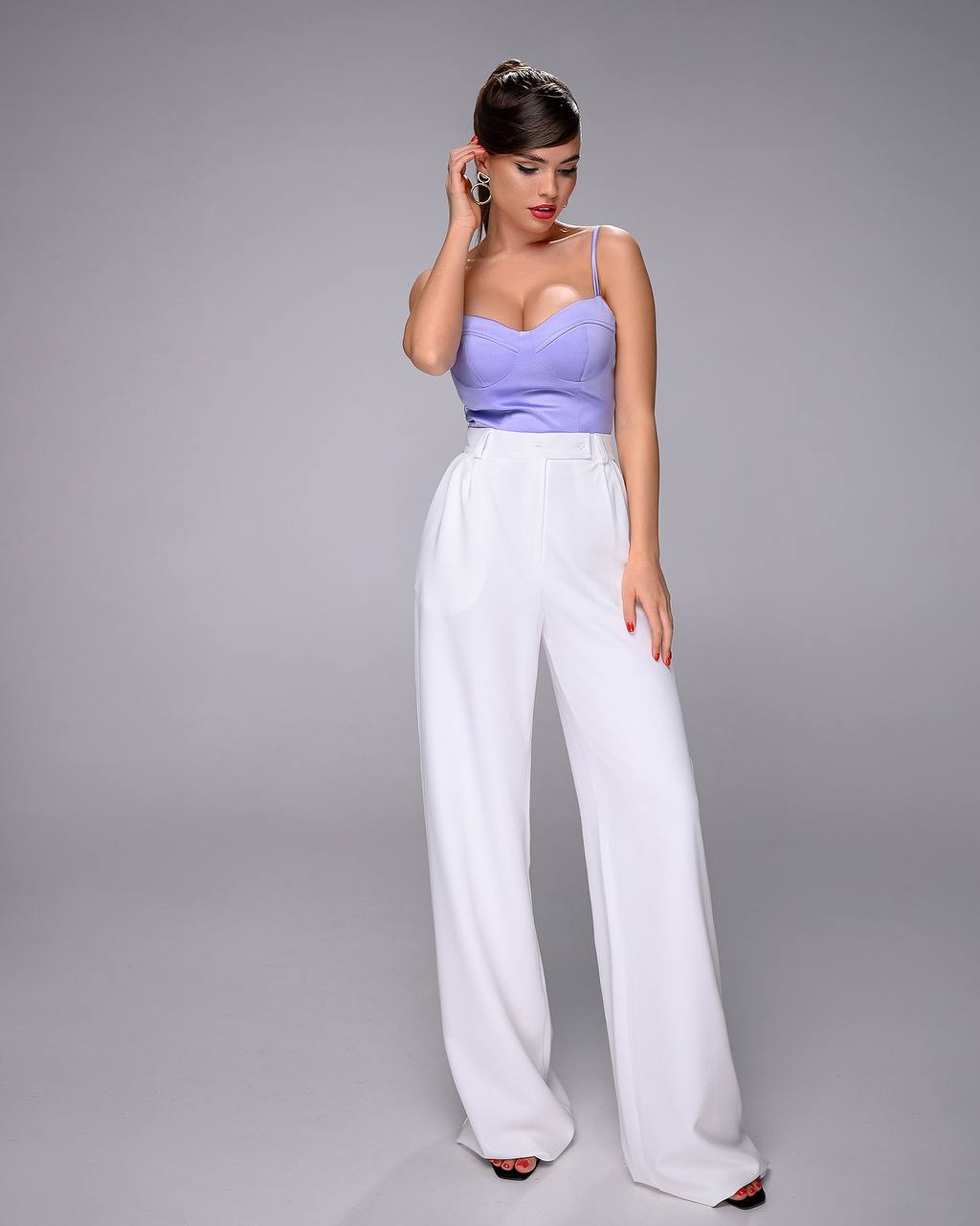 Woman wearing a purple top and white pants on a gray background