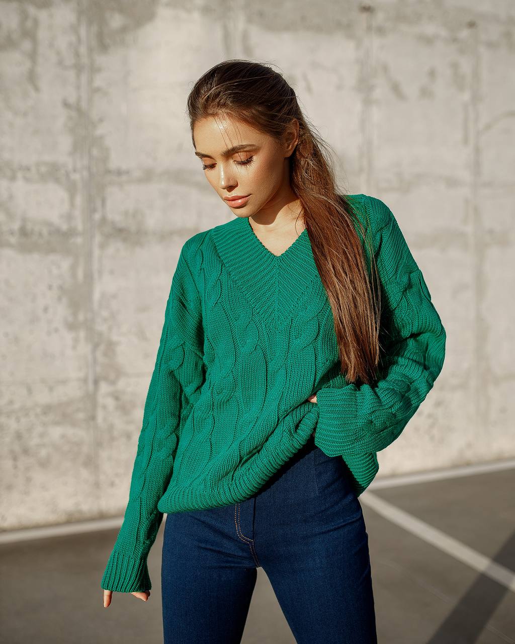 Woman wearing a green cable knit sweater against a textured wall.