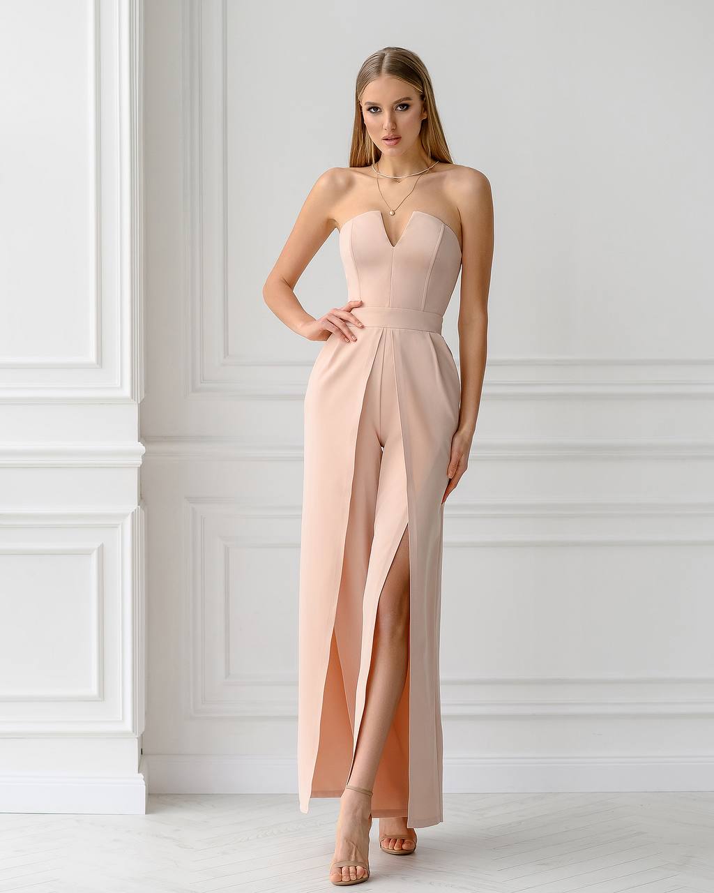 Woman wearing a strapless pink jumpsuit with a high slit in a minimalistic setting