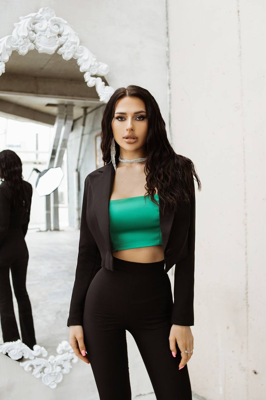 Woman in a green top and black blazer standing in an urban setting with white flowers.