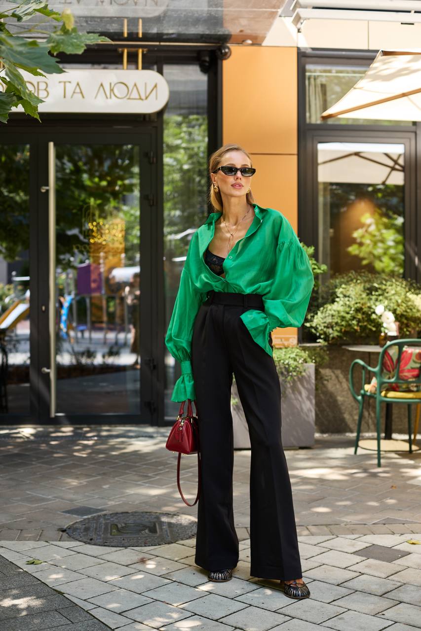 Woman in green shirt and black pants standing on a street with storefronts in the background