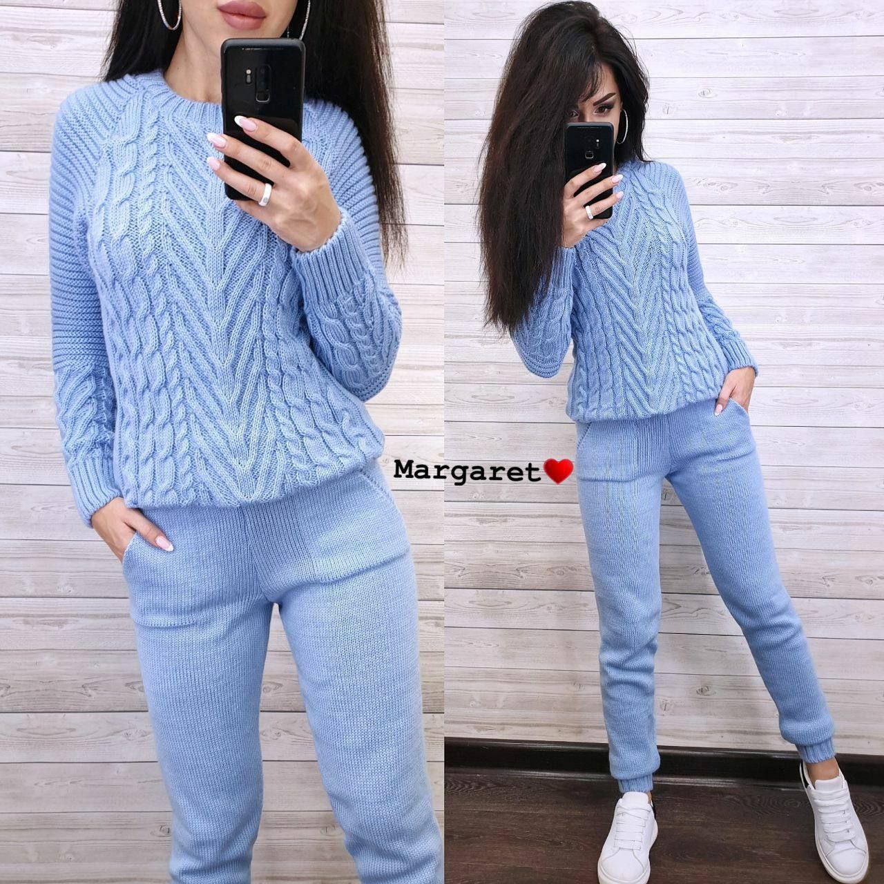 Woman wearing a light blue cable knit sweater and pants, taking a mirror selfie.