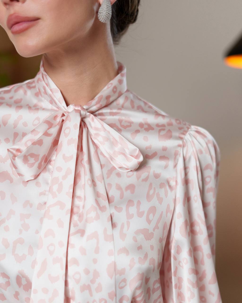 Close-up of a person wearing a pink leopard print blouse with a bow detail.