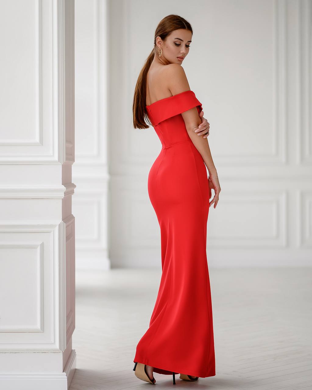 Woman wearing a red off-shoulder gown in a white room