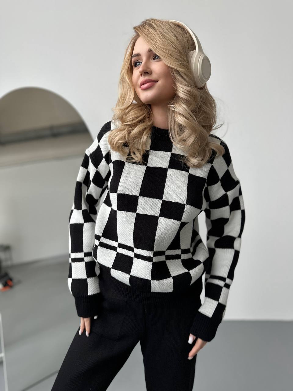 Woman wearing a black and white checkered sweater and headphones indoors.