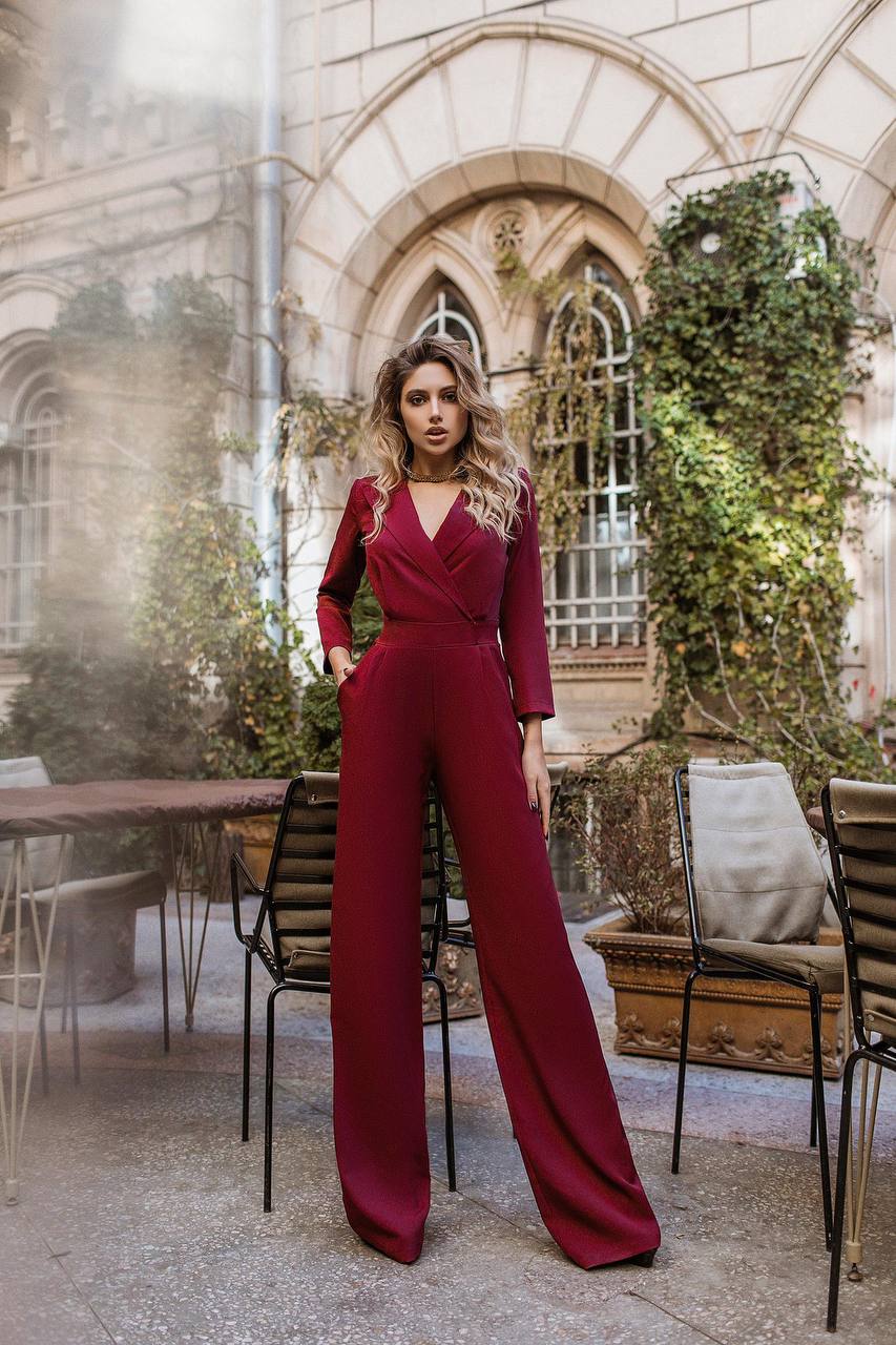Woman in a red jumpsuit standing in an outdoor setting with architectural elements and greenery.