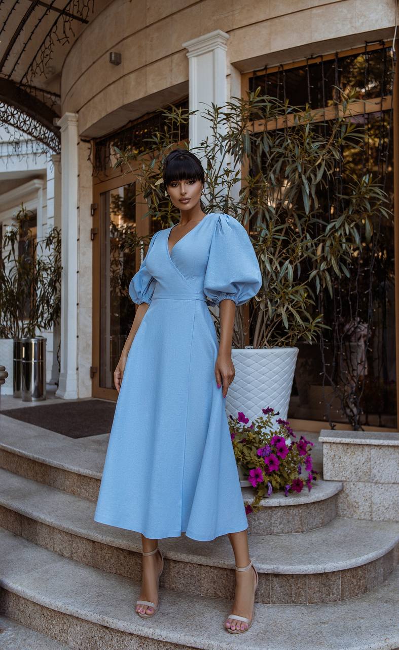 Woman in a light blue dress standing on steps with plants and flowers in the background