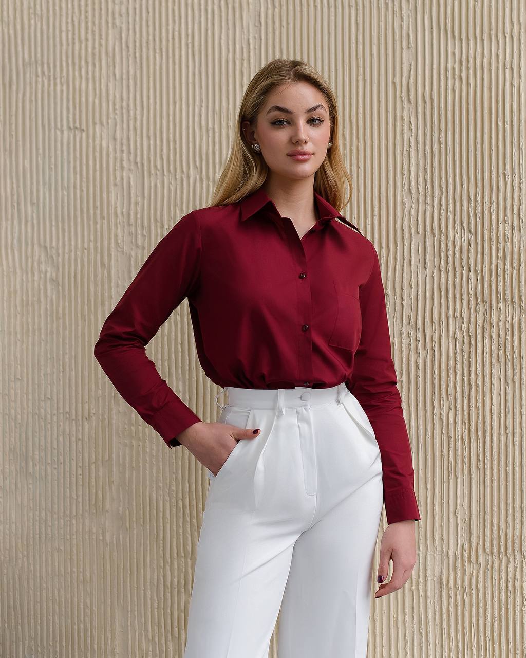 Woman wearing a red blouse and white pants against a beige textured wall