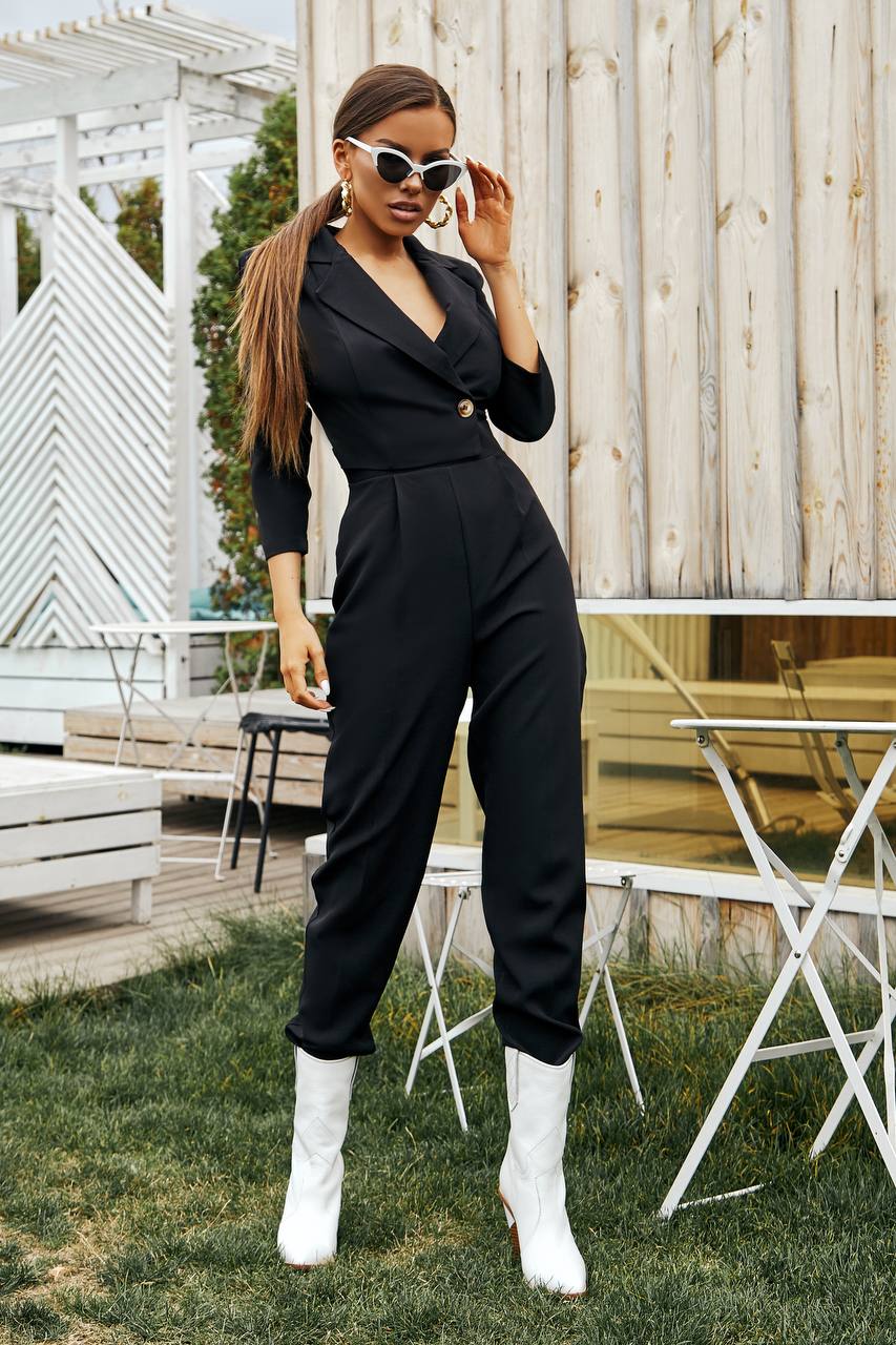 Woman in a black jumpsuit with white boots standing outdoors.