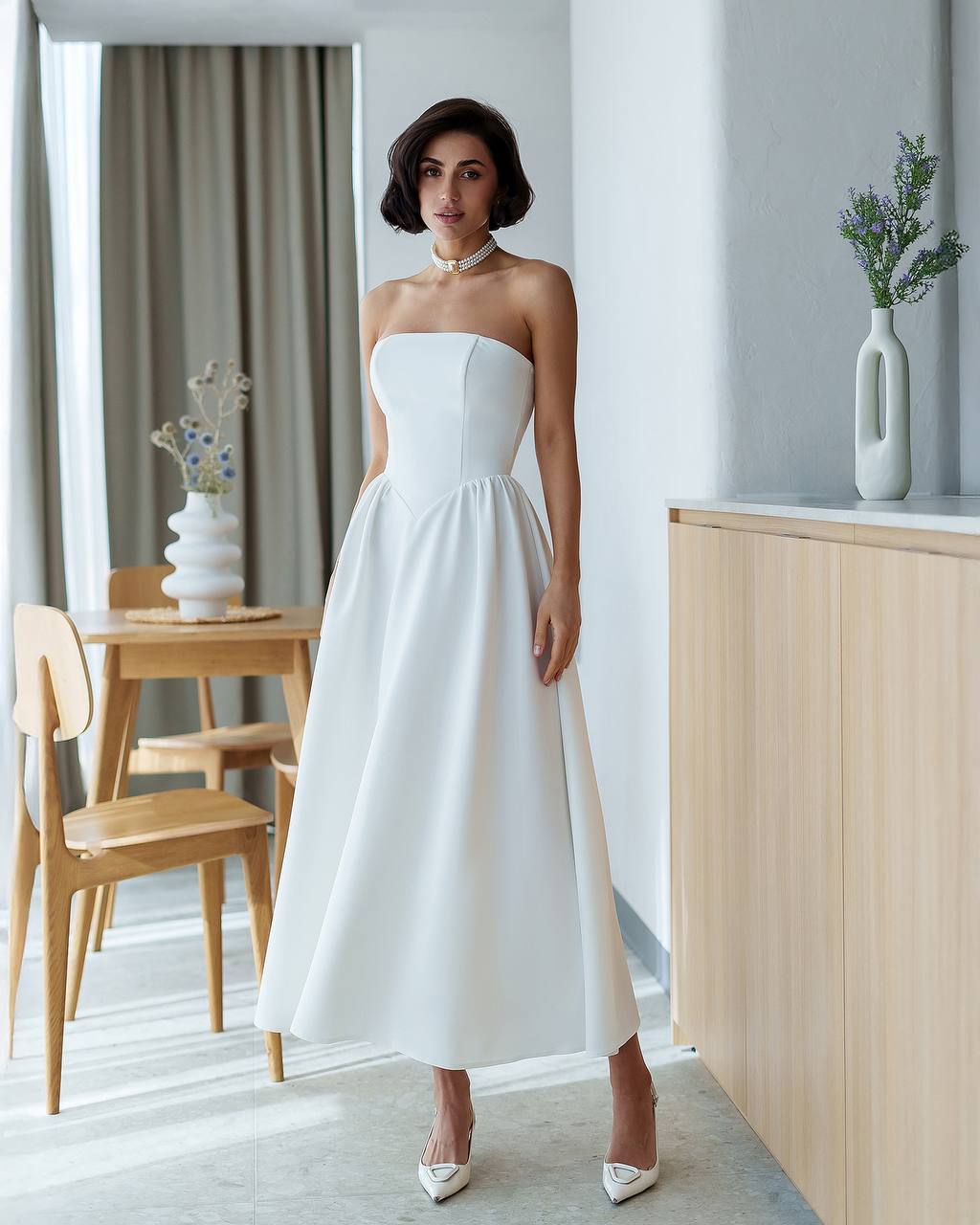 Woman in a white strapless dress standing in a modern interior setting.