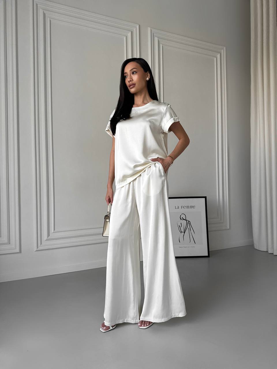 Woman in a white outfit standing in a minimalistic room with gray walls and a gray floor.