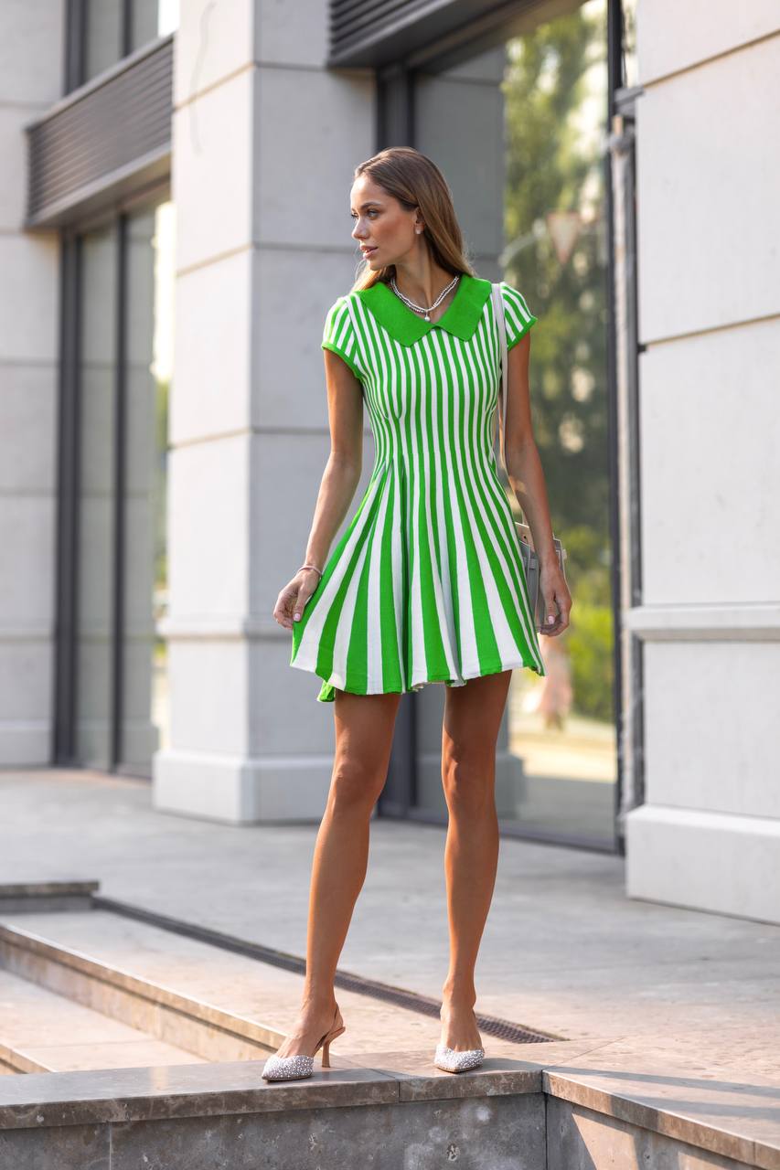 Woman in a green and white striped dress standing outdoors near a building.