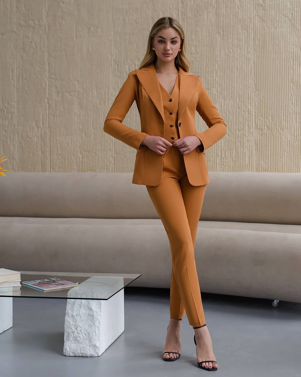 Woman in a mustard yellow suit standing in a modern living room.