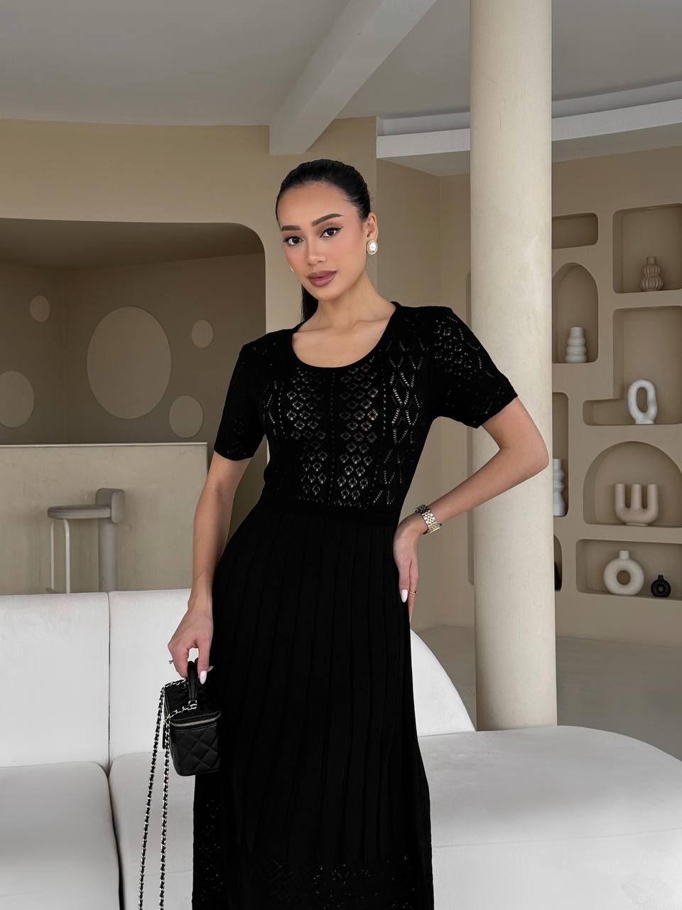 Woman in a black dress holding a handbag in an indoor setting