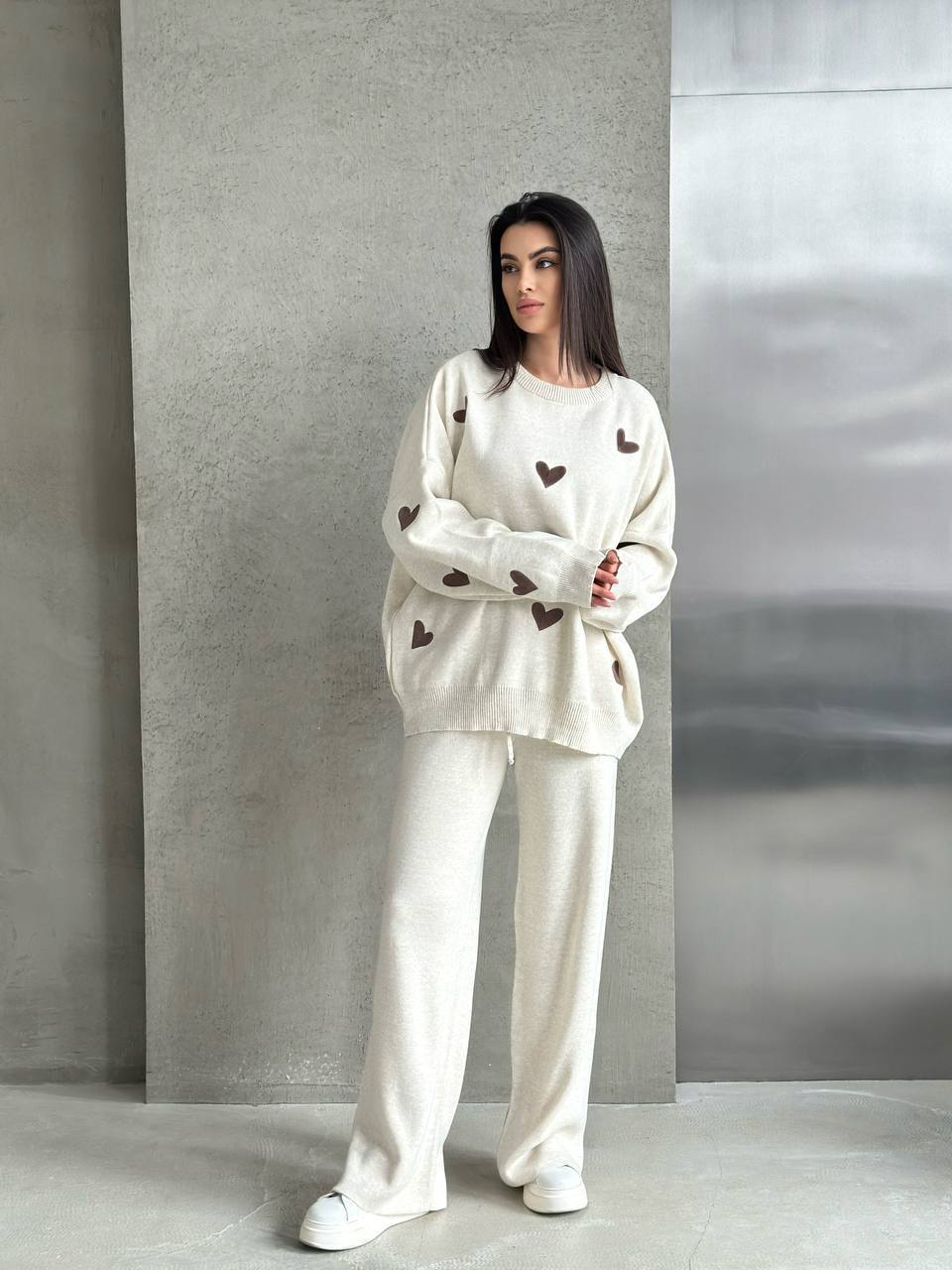 Woman wearing a white outfit with heart patterns against a gray wall.
