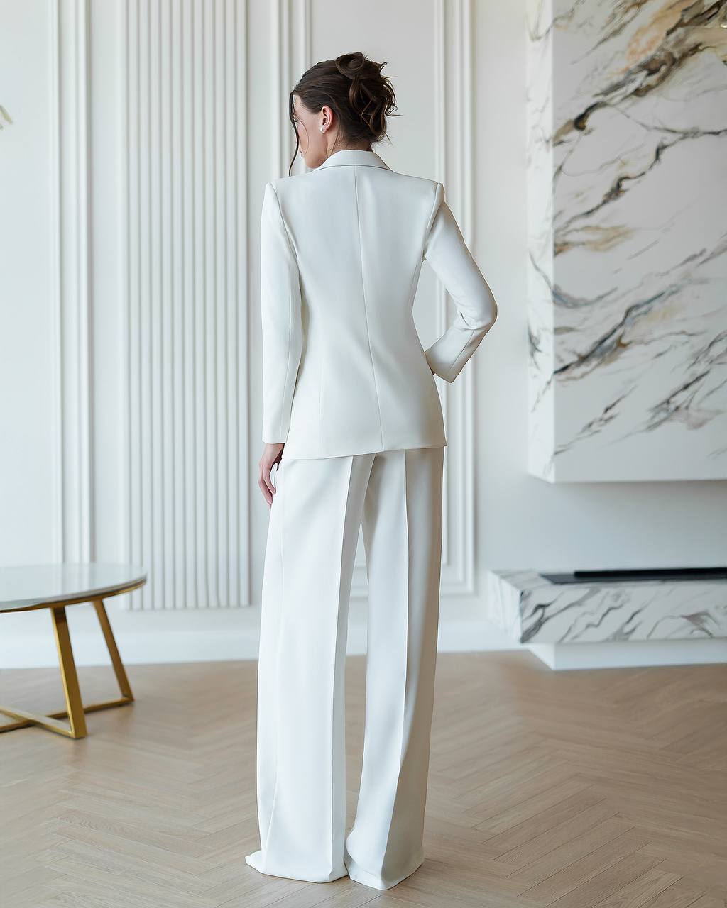 Woman in a white suit standing in a stylish room with marble wall.