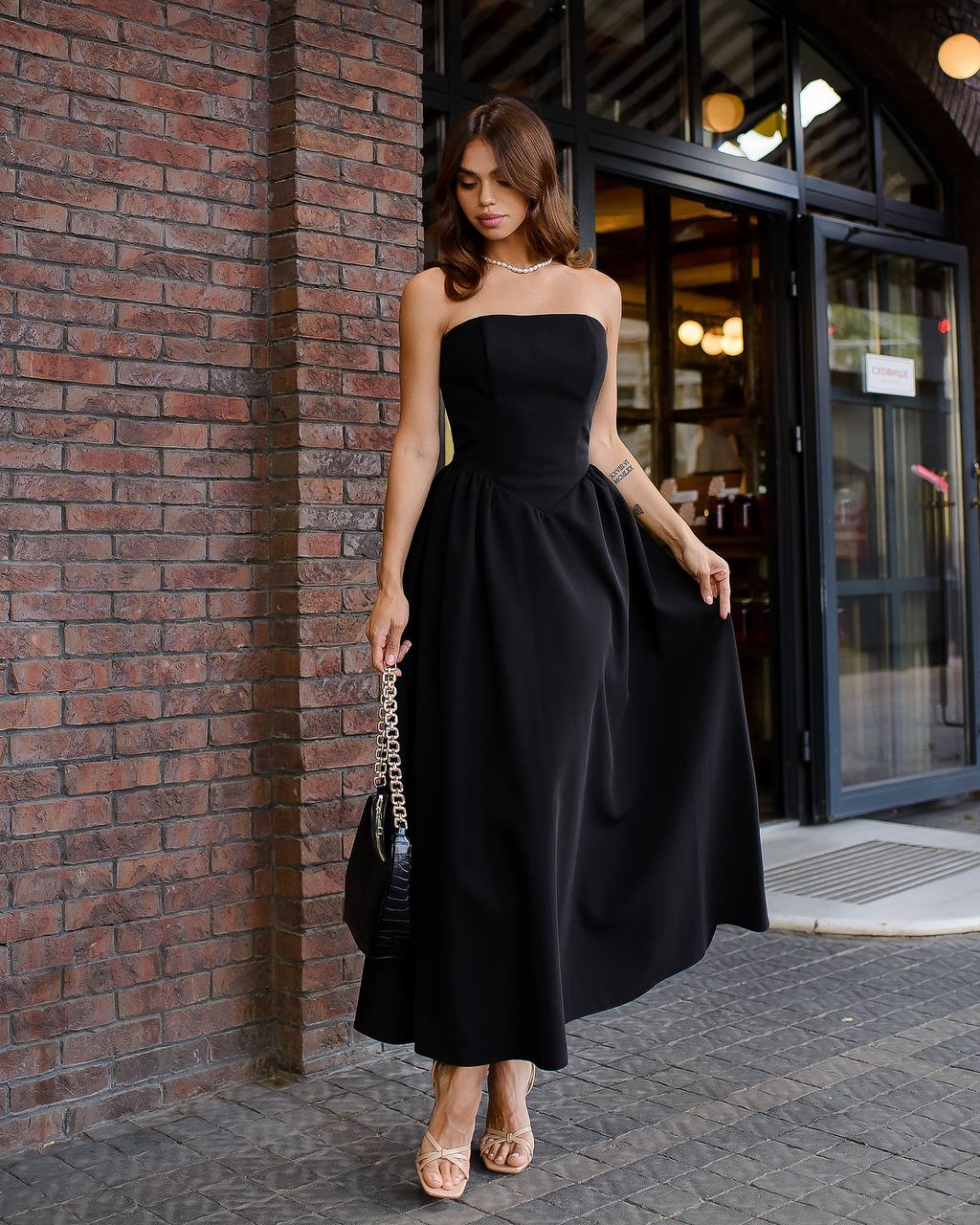 Woman in a black strapless dress standing against a brick wall.