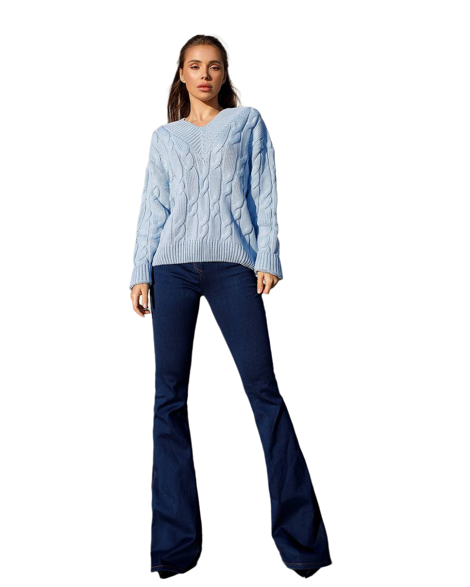 Woman wearing a light blue cable knit sweater and dark blue flared jeans on a white background