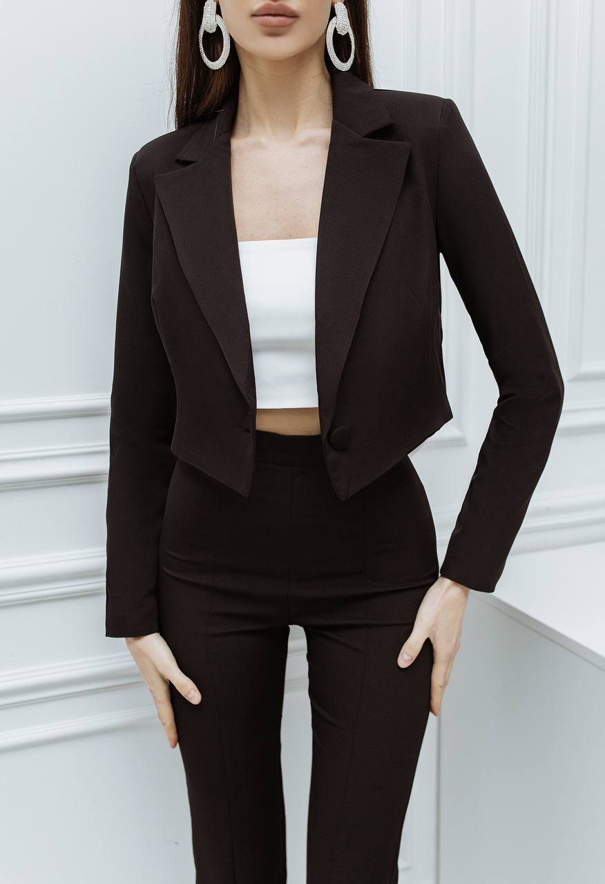 Person wearing a black suit with a white top against a light-colored wall.