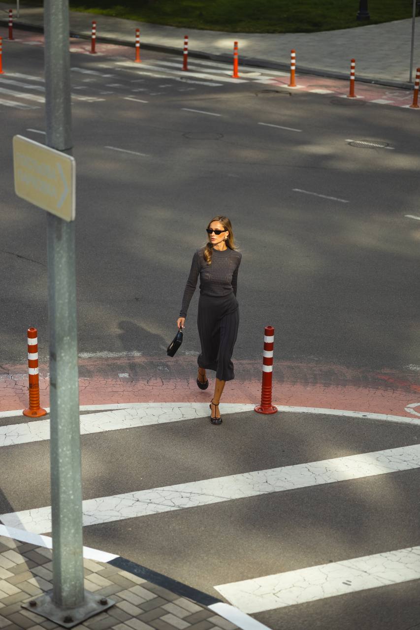 Woman walking on a crosswalk with traffic cones and a street sign in the background