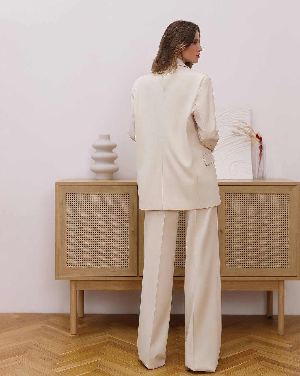 Woman in a beige suit standing in front of a wooden cabinet with wicker doors.
