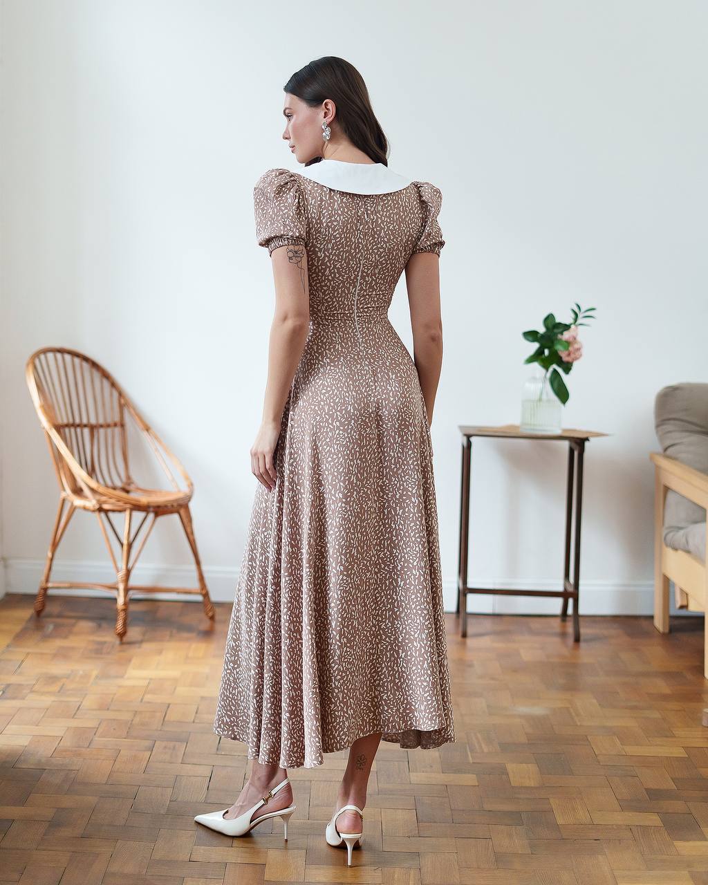 Woman wearing a patterned dress in a room with wooden flooring and minimal decor.