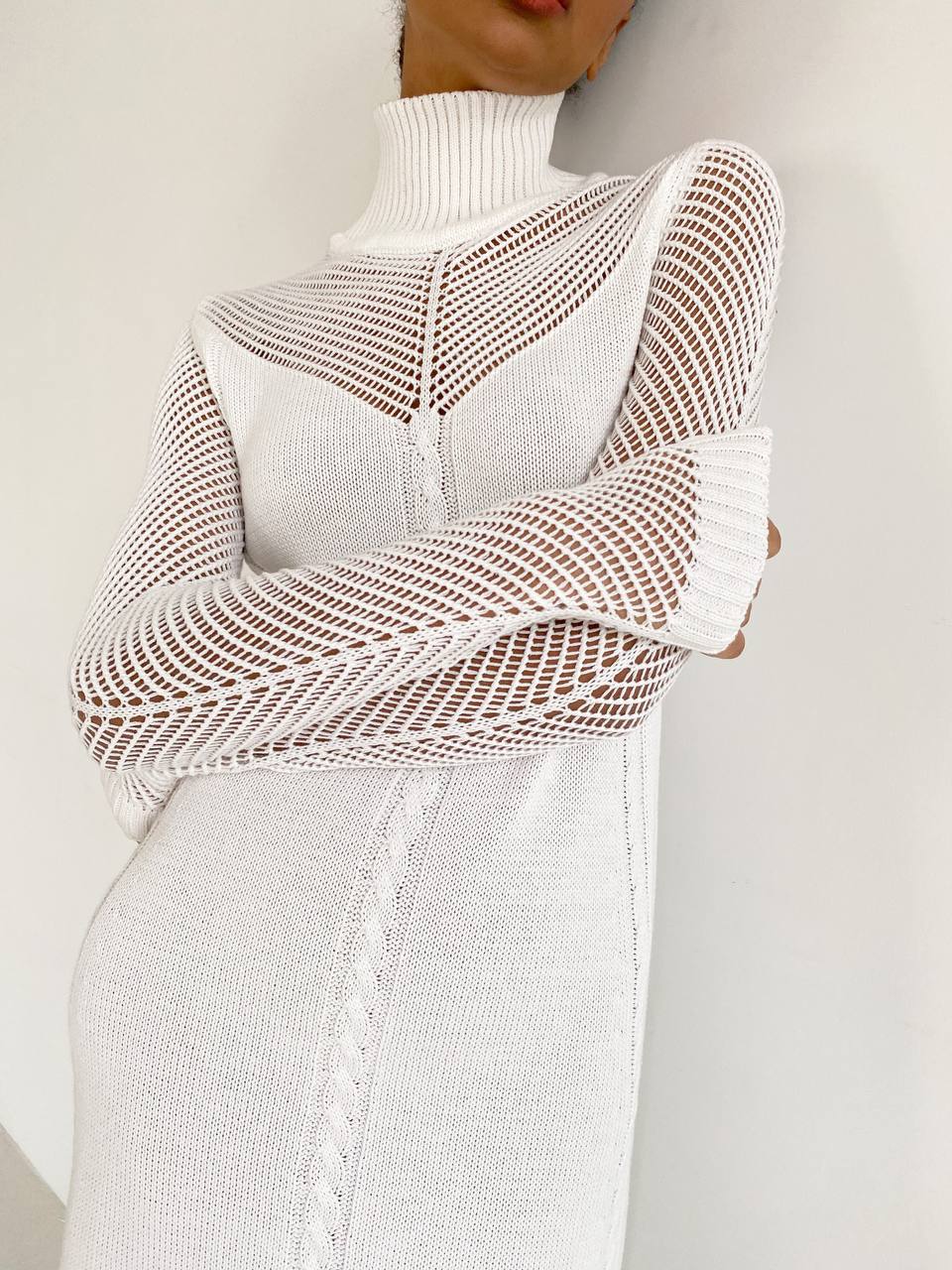 Person wearing a white knit sweater with a unique pattern on a plain background