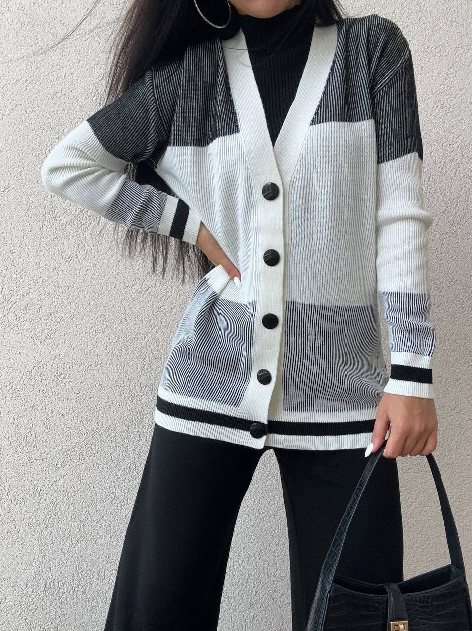 Person wearing a black and white striped cardigan with buttons, holding a black handbag against a light background.