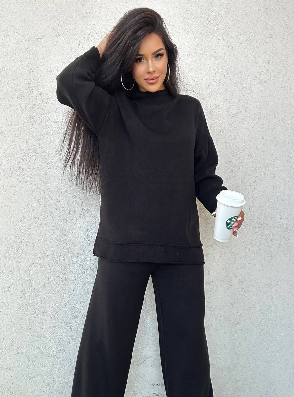 Woman in black outfit holding a Starbucks cup against a light gray background