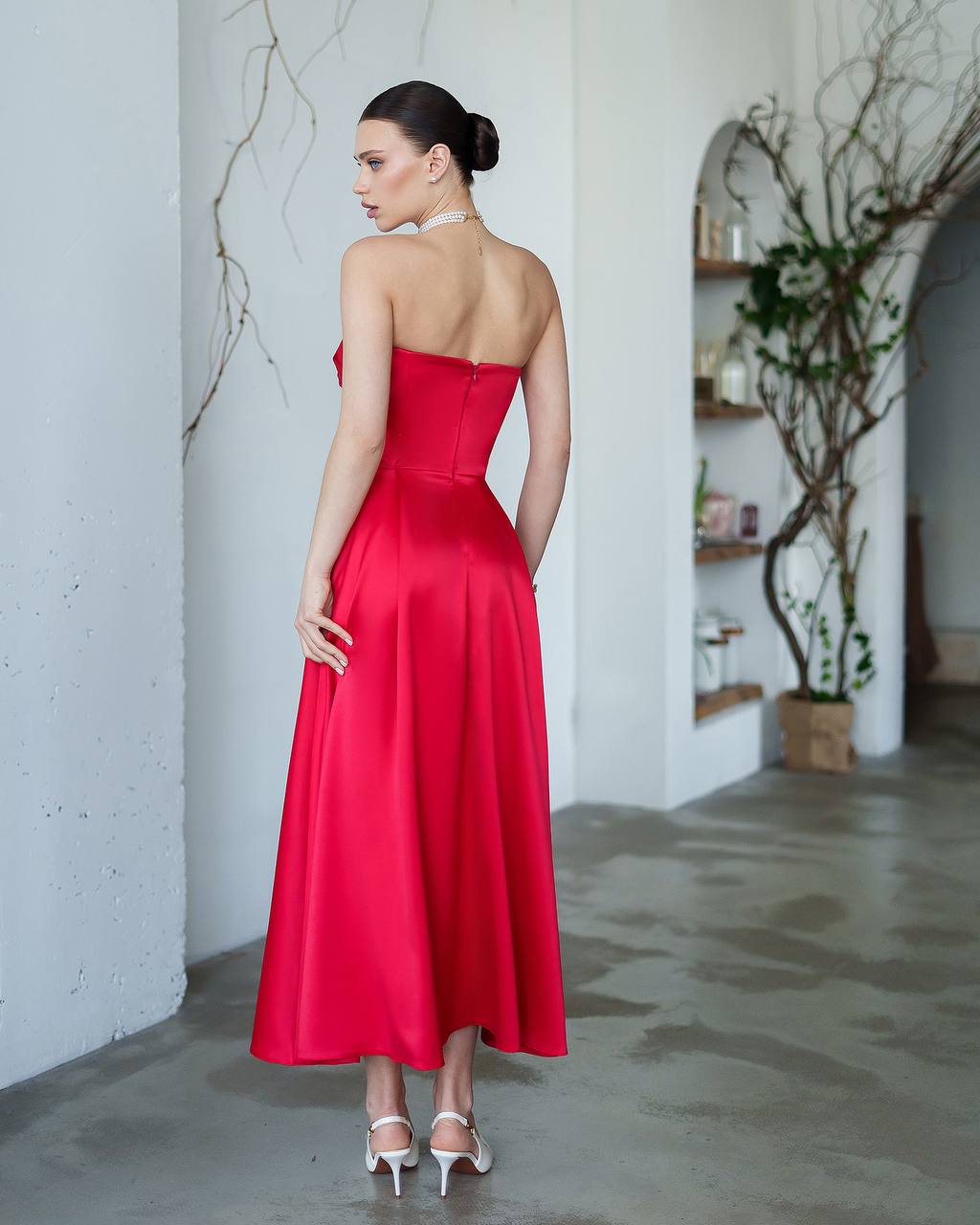 Woman in a red strapless dress standing in a room with white walls and a plant.