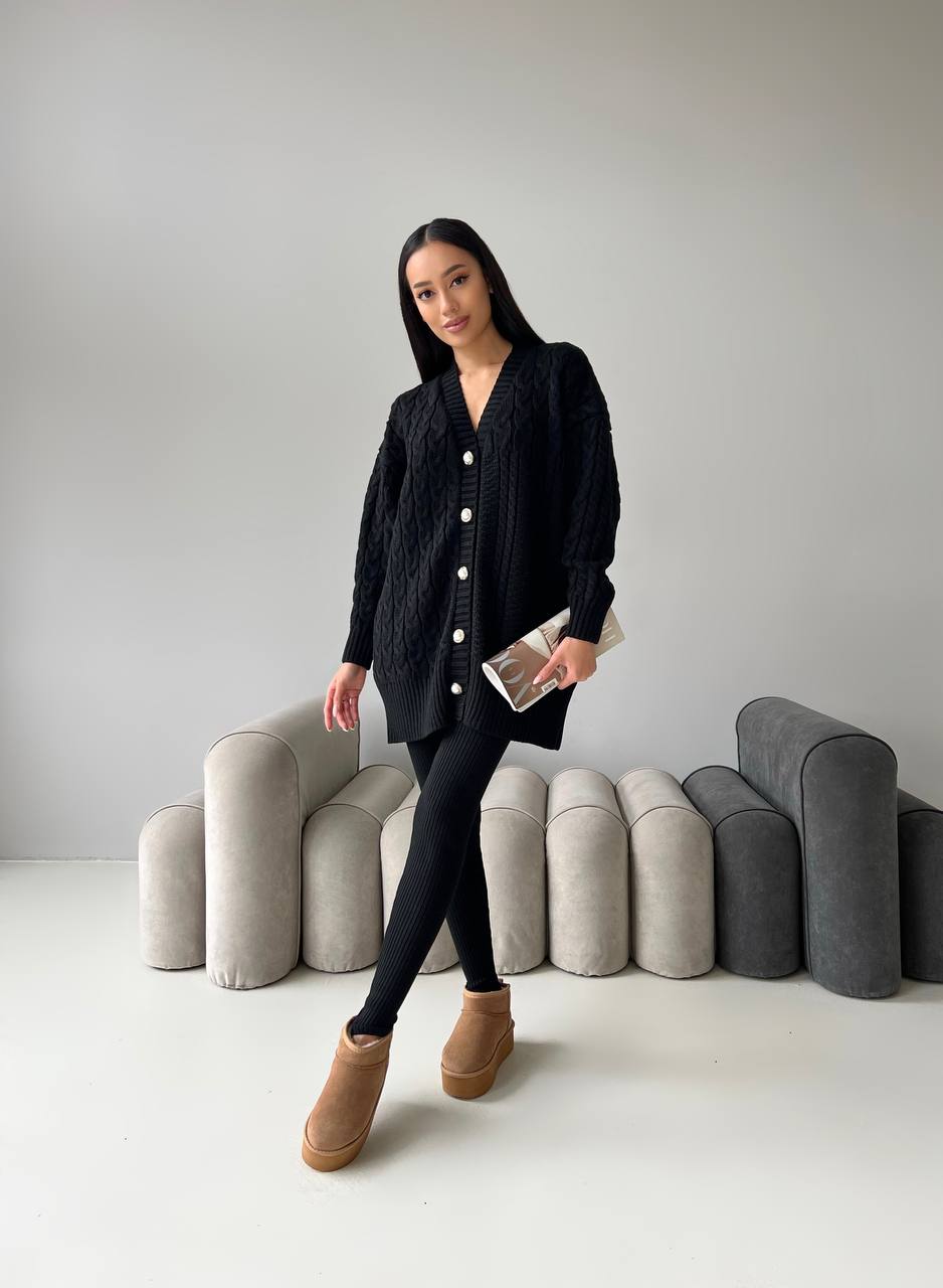 Woman in a black cardigan standing in front of modern, curved furniture against a plain background