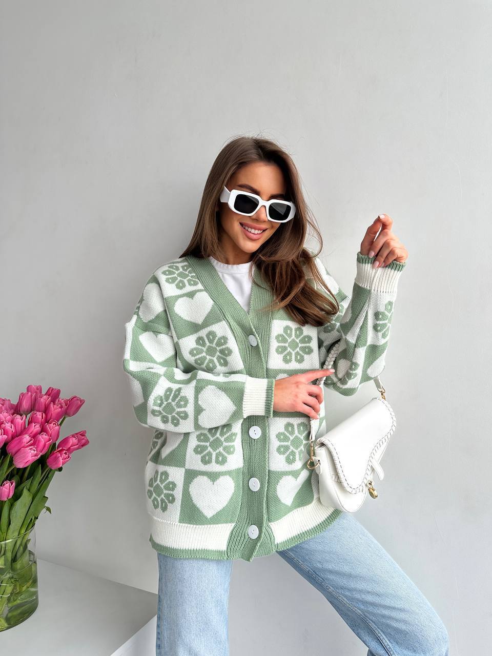 Woman wearing a green and white patterned cardigan with a vase of pink tulips in the background.